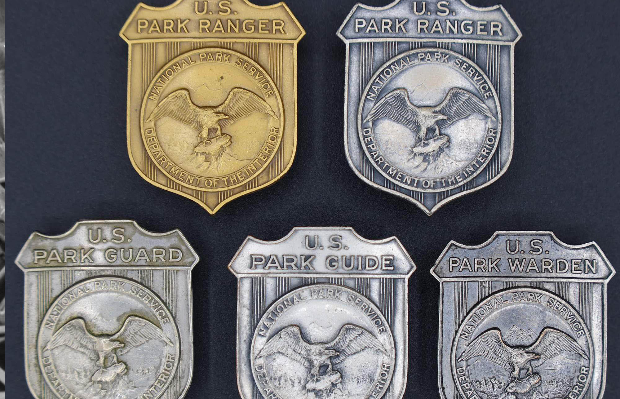Shield-shaped badges with left facing eagle in the middle. Gold and silver marked U.S. Park Ranger, others marked U.S. Park Guide, U.S. Park Guard, and U.S. Park Warden.